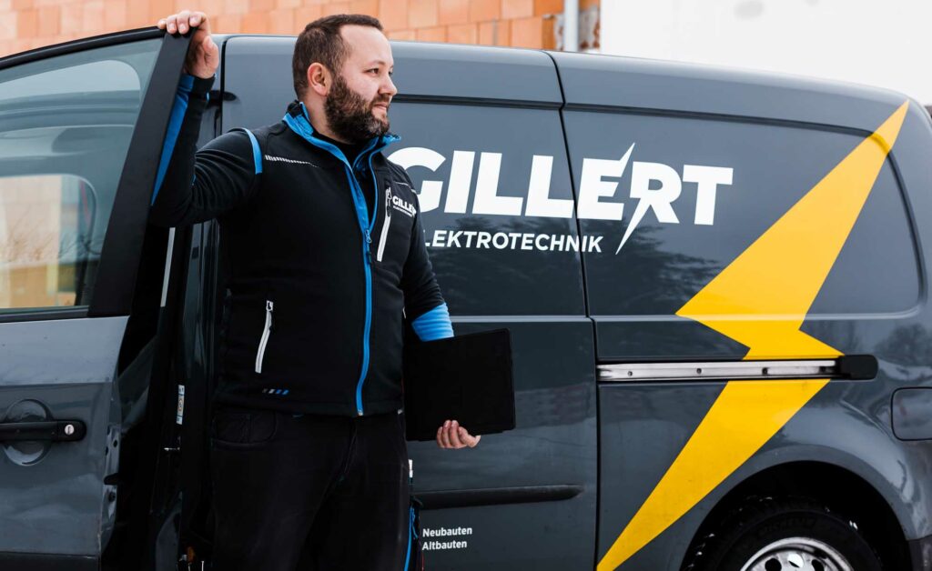 Elektriker mit Tablet vor Firmenwagen.