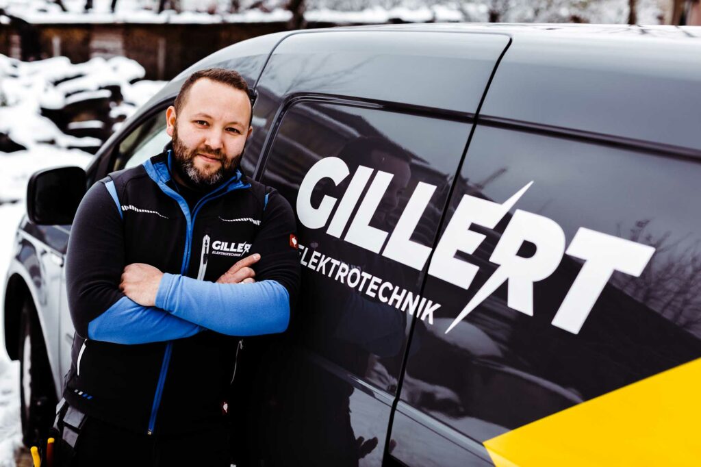 Elektriker posiert neben Firmenwagen.